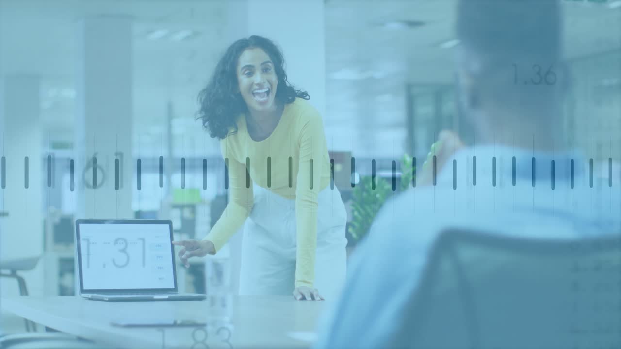 woman leaning over table in business hub, pointing at laptop showing animated chart overlays