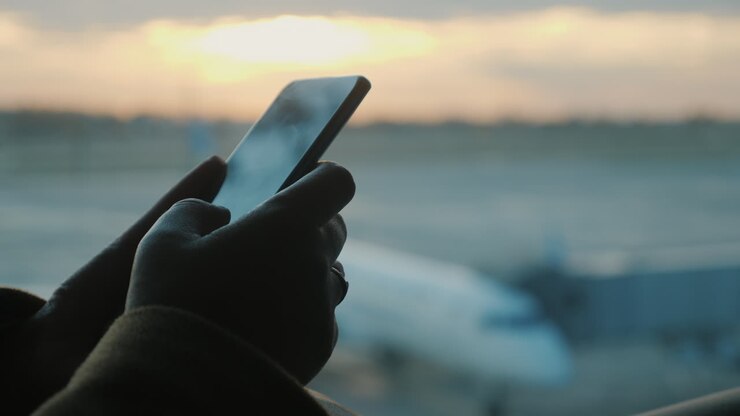 Passenger hands with a smartphone. In the background, a window and planes