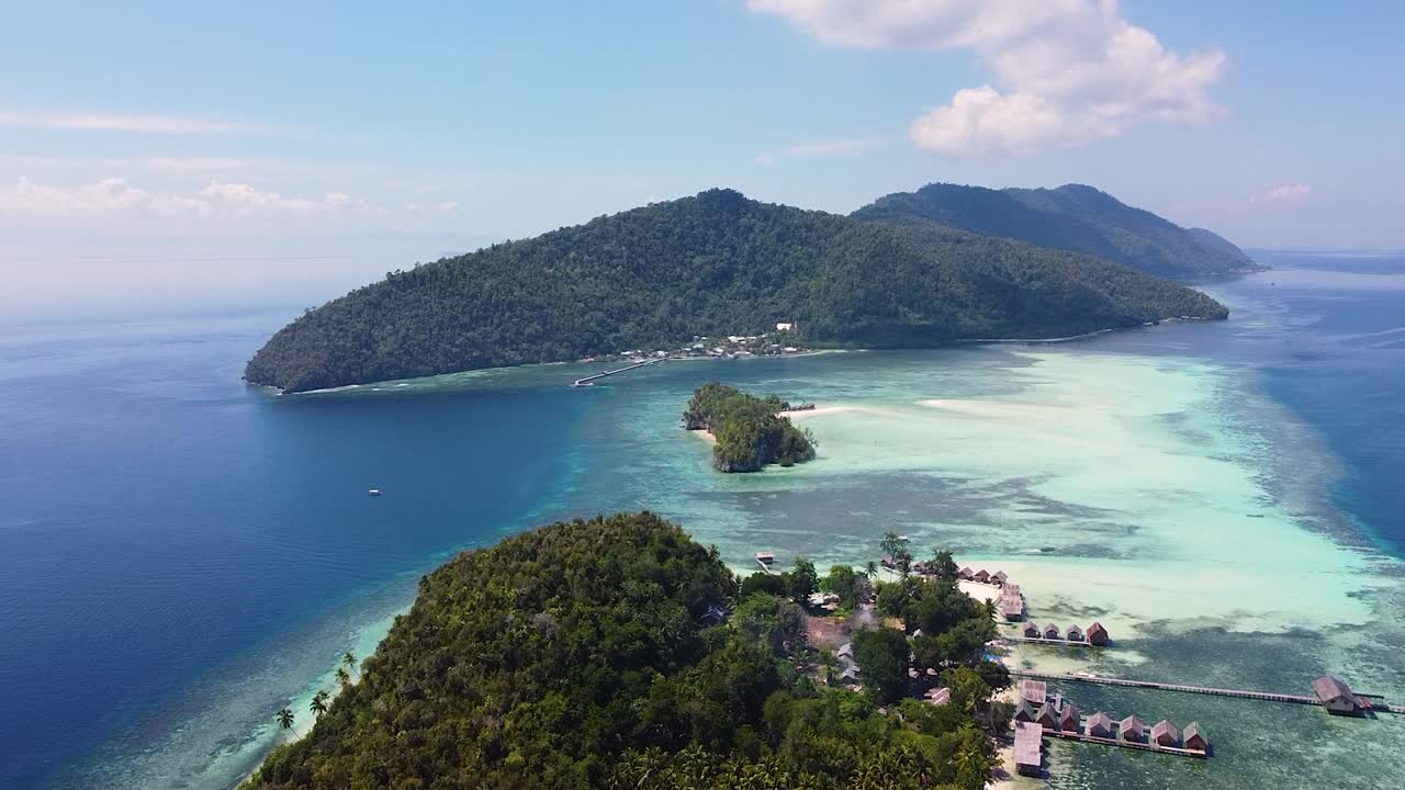 panorámica vista aérea que se eleva sobre el alojamiento de la cabaña de playa remota en una isla tropical rodeada de arrecifes de coral y aguas cristalinas del océano en raja ampat, papúa occidental, indonesia