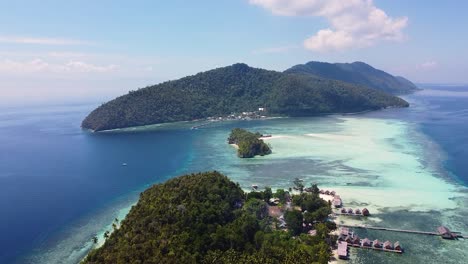 scenic aerial view rising over remote beach hut accommodation on tropical island surrounded by coral reefs and crystal clear ocean water in raja ampat, west papua, indonesia