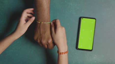 sister ties rakhi on brother next to chroma key mobile cell phone