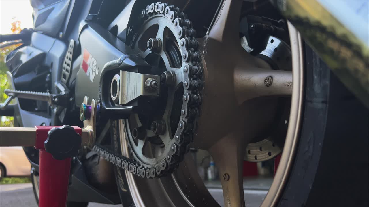 primer plano de rociar lubricante de la lata de aerosol en la cadena de la motocicleta