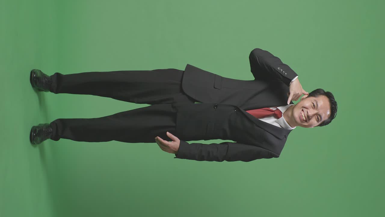 아시안 사업가의 몸은 따뜻하게 미소 짓고 스튜디오에서 녹색 화면 배경에 전화 제스처에 대화하고 있습니다.