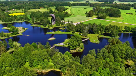 green landscape and deep blue water of kirkliai lake with observation tower, aerial orbit view