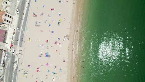 people bathing and sunbathing on beach of sesimbra, portugal. aerial top-down forward