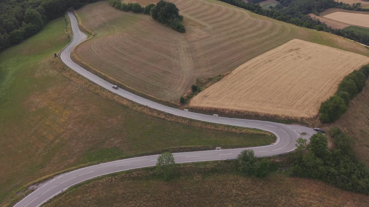 Una suggestiva veduta aerea di una strada di campagna tortuosa che attraversa campi agricoli ondulati e macchie di foresta.