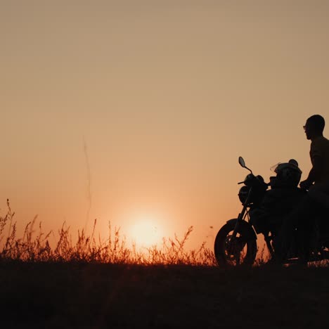 a young romantic couple stands by a motorcycle at sunset