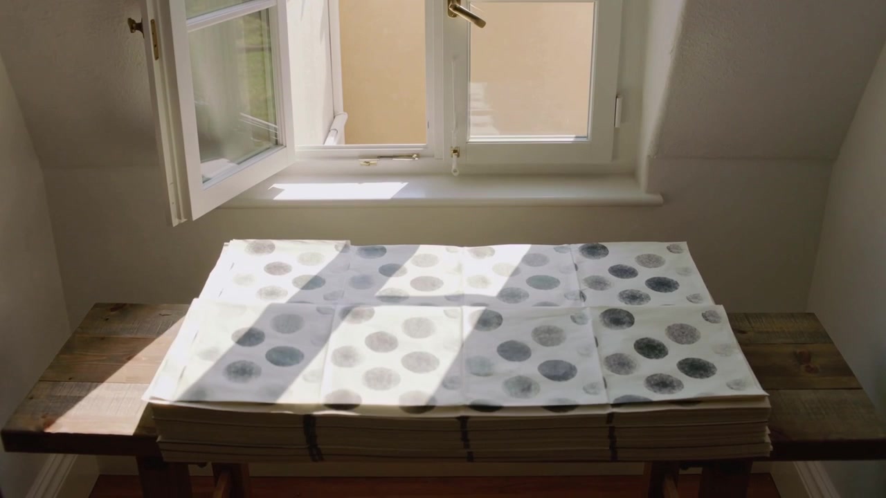 Lifting top sheet open window breeze carrying dotted paper across wooden bench, sunlight shifting