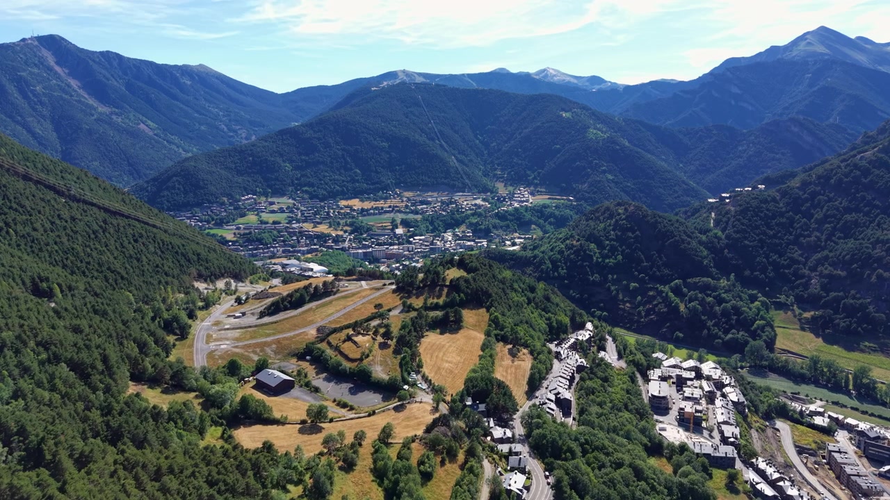 Valle di Ordino ad Andorra con una città di montagna annidata tra le verdi cime boscose dei Pirenei, edifici residenziali, campi aperti e strade tortuose sotto un cielo estivo azzurro