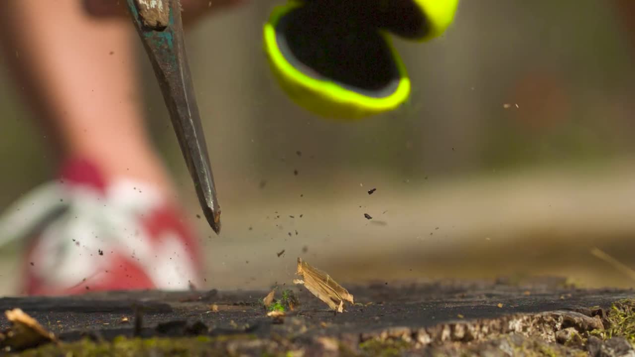 A yellow tennis ball being cut in half by an axe during the summer time while the sun is shining