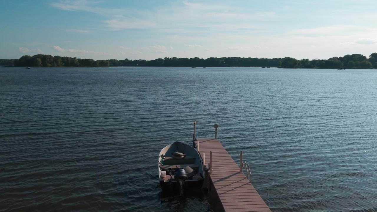 Plano aéreo baixo sobrevoando um barco de pesca atracado durante o verão em um lago em Center City, Minnesota. 4K