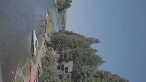 Small-boats-on-the-shore-of-a-tranquil-river-with-houses-and-forest-in-Patagonia,-Argentina