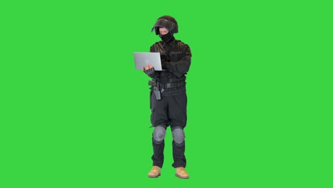 masked police officer using a laptop computer on a green screen, chroma key