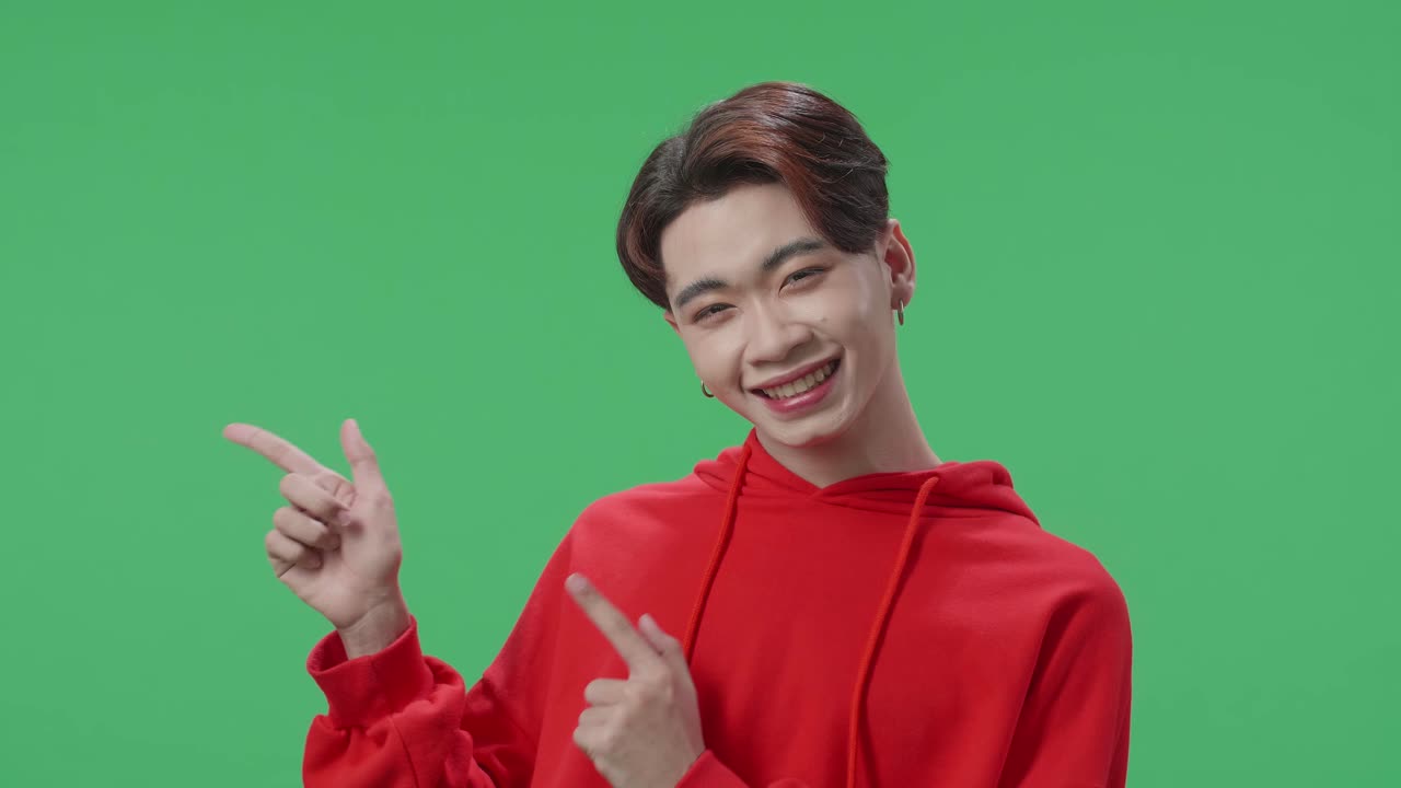 The Inspired Asian Transgender Male Smile And Pointing To The Side While Standing In The Green Screen Studio