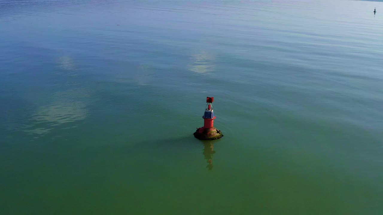 Aerial orbit flying over orange navigational aid marker on calm sea water