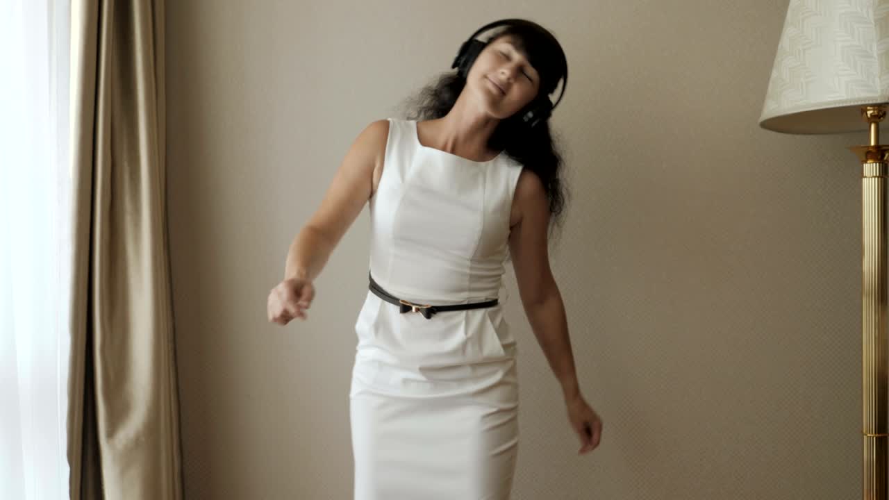 joven feliz bailando y divirtiéndose en la habitación escuchando música en auriculares inalámbricos. mujer de negocios disfrutando de la danza, divirtiéndose de la fiesta. baile de hilo viral, hilo dental. tecnología.
