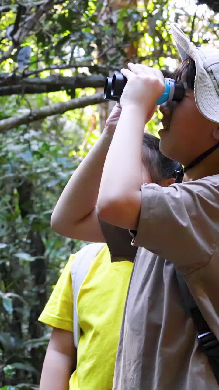 Un ragazzo e una ragazza asiatici esplorano una foresta lussureggiante con il binocolo sotto una luminosa luce solare naturale