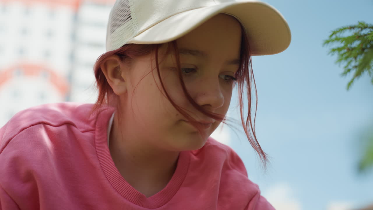 Girl Inspecting Tiny Object Outdoors, Young Female Carefully Examining Tiny Object Amid City Surroundings, Youthful Girl Studying Miniature Object Placed On Bench With Urban Scenery Around