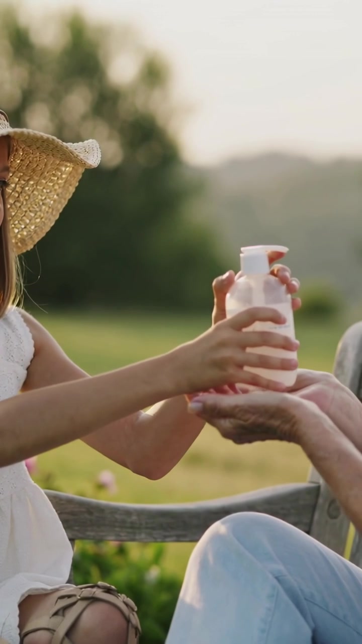 Vertical video: Adult cupped hands cueing child white dress pumping sunscreen into palms in park