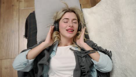 A-smiling-woman-falls-on-a-bed-in-headphones-and-listens-to-music
