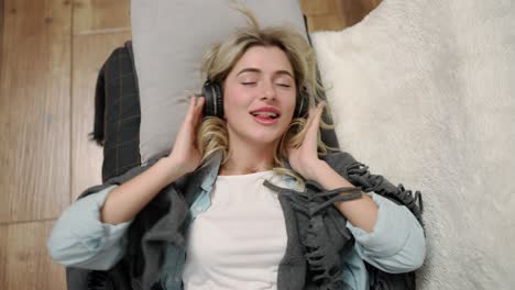 a smiling woman falls on a bed in headphones and listens to music