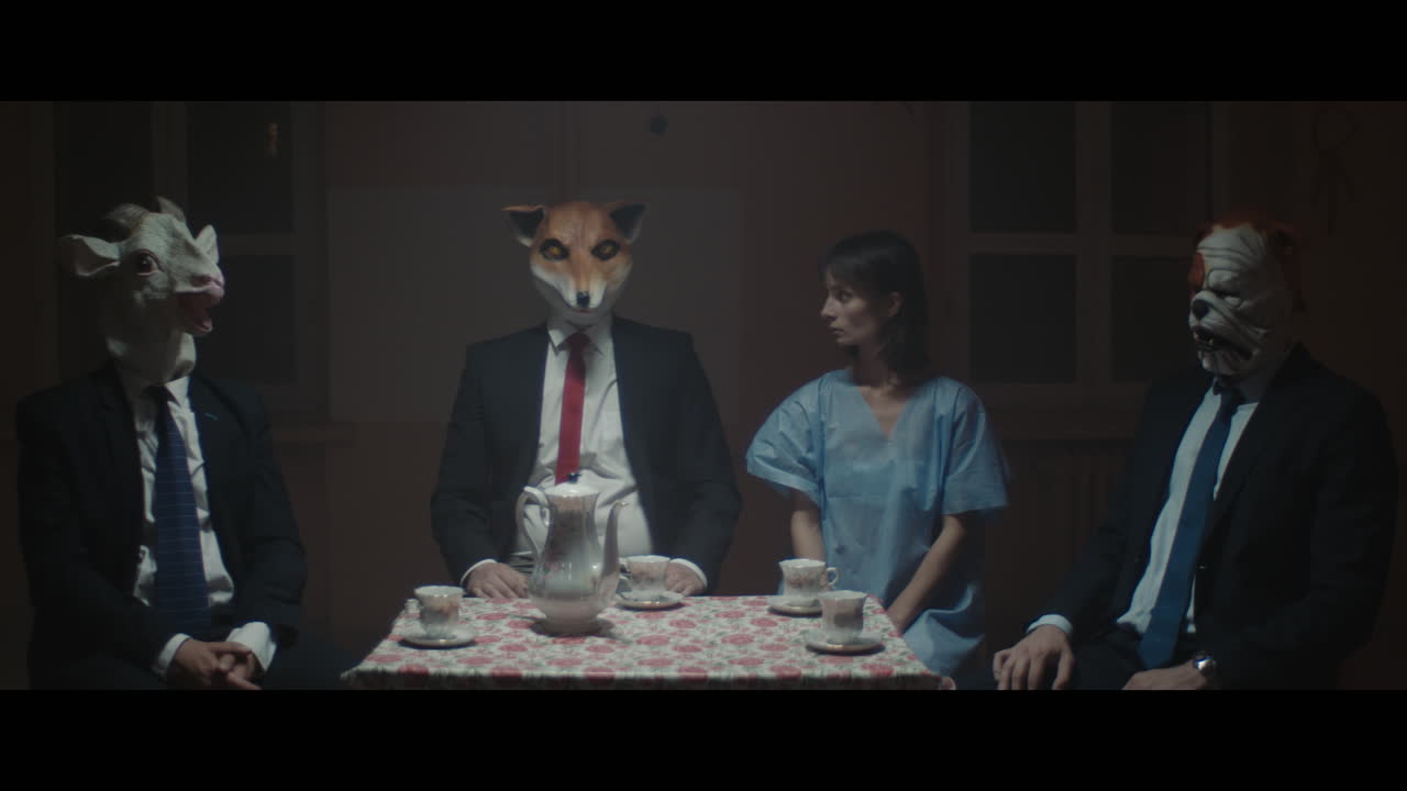 A girl sits at a table with strange figures in animal masks.