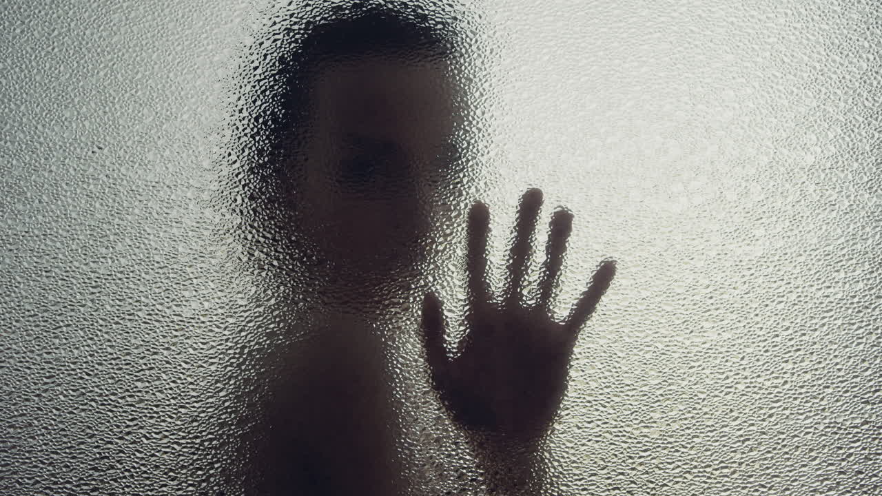A female silhouette behind the frosted window touches the glass slowly