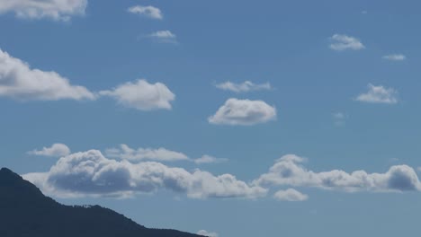 Filming-with-a-drone-in-167mm-the-passage-of-beautiful-white-clouds-with-shadows-in-the-lower-parts-in-a-striking-sky-and-seeing-the-top-of-a-mountain-everything-is-very-calm