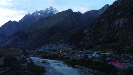 A-drone-shot-of-a-small-scenic-remote-village-on-the-banks-of-river-Baspa-with-the-snow-peaks-of-Indian-Himalayas-in-the-background