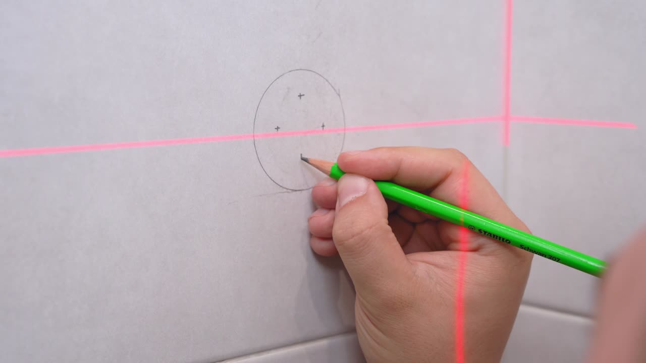 el artesano ha dibujado un círculo con lápiz y está haciendo marcas de x en la pared para fijar estantería o muebles. el haz láser de recta electrónica detectó líneas rectas.