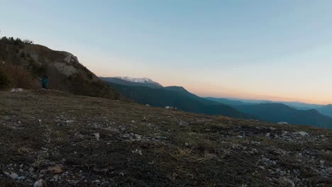 Young-girl-running-with-a-black-labradot-dog-on-a-mountain-at-sunset-during-autumn