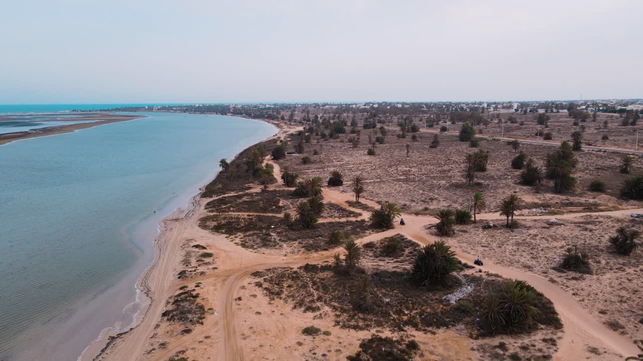 una vista aérea de una playa, con el océano y la costa arenosa visibles en la laguna de djerba en túnez, atv quad en un camino de tierra que cruza la zona