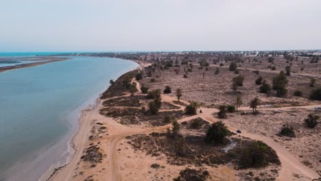 An-aerial-view-of-a-beach,-with-the-ocean-and-sandy-shoreline-visible-in-the-Lagoon-of-Djerba-at-Tunisia-,-ATV-quad-on-A-dirt-pathway-that-crosses-through-the-area