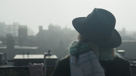 woman in hat watching medieval city rooftops in misty morning