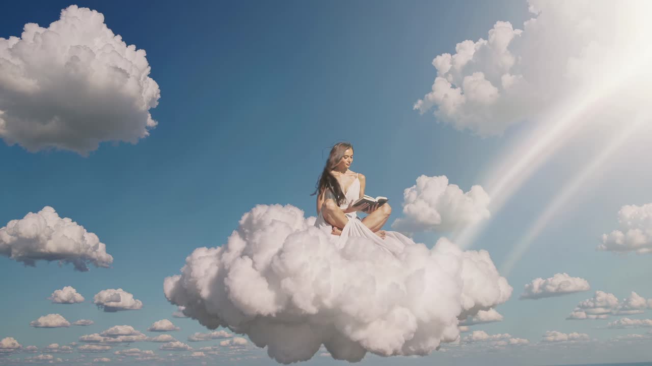 Aerial video shot of a woman in a flowing dress reading a book while seated on clouds, set