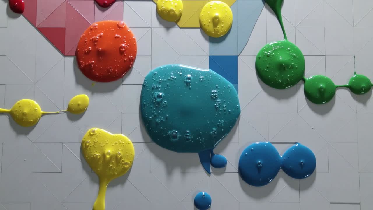 泡を伴いながら重力によって垂直の格子パネルを下へ広がる中央のシアンが、絵の具のしずくを引きずる様子。