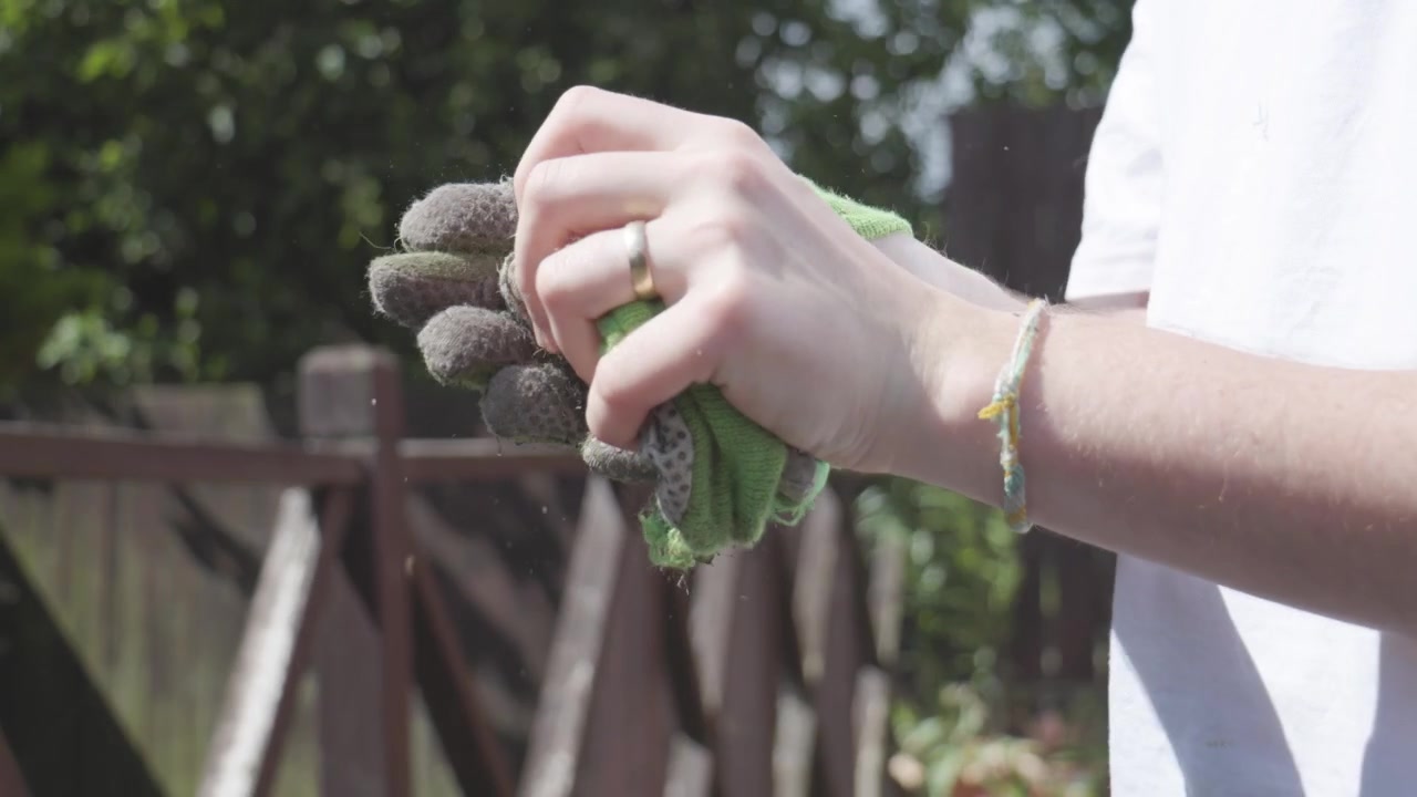 Green gardening gloves being removed in close up outdoors, showing dirty fabric and hands after yard work. Practical garden safety, cleanup routine, weekend home gardening.
