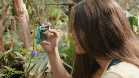 niña de la naturaleza tomando una foto de una mariposa usando un teléfono inteligente en un santuario de vida silvestre aprendiendo el hábitat natural disfrutando de una excursión al zoológico compartiendo la conciencia ambiental en las redes sociales 4k
