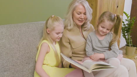 grandmother sitting on sofa with her two granddaughters and reading them fairy tales