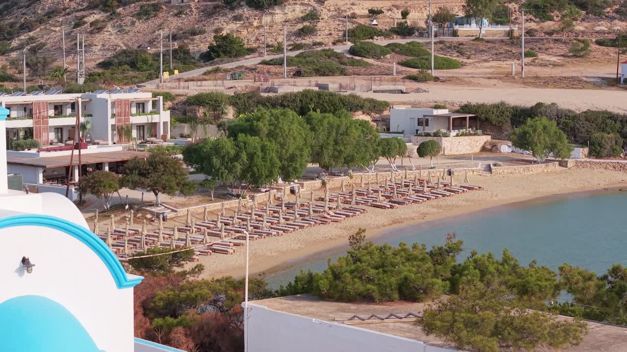 Cinematic drone capture of the white chapel at Amopi, Karpathos, revealing the golden beach and turquoise sea in the background