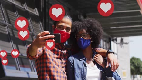 video of falling icons over diverse man and woman wearing face masks and using technology