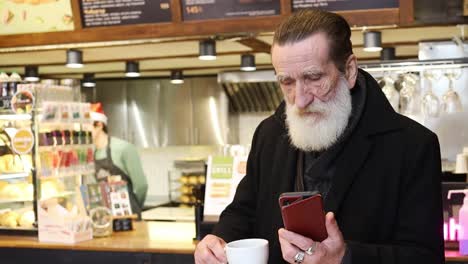 a bearded man sips coffee absorbed in his phone reflecting calm a bearded man sits cozily sipping coffee and absorbed in his phone he contemplates while glancing at his wallet merging relaxation with connectivity