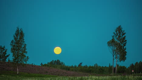 luna dorada avanzando sobre un cielo azul y un paisaje verde con árboles