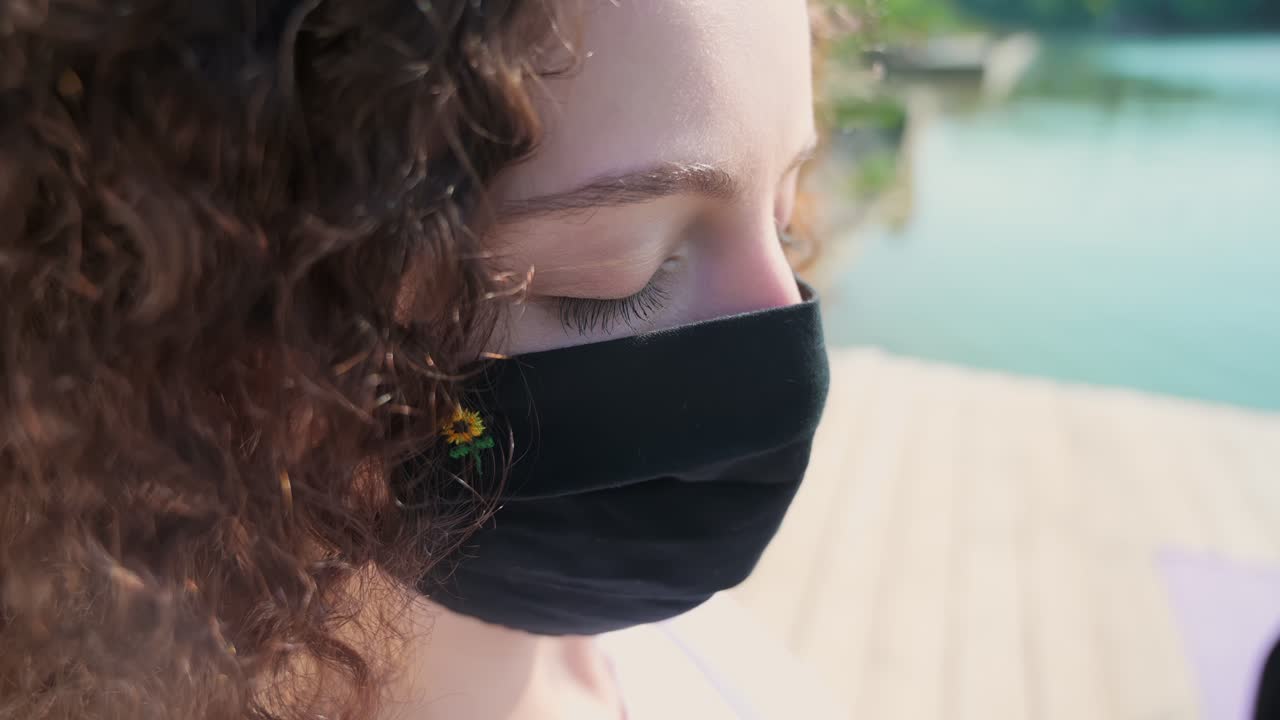 Two young curly women practicing yoga on the mats while wearing black protective mask. Park and lake in background. Sunny day. Corona Virus idea. Chisinau, Moldova