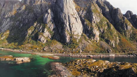 Aerial-shot-of-a-white-camper-van,-on-a-coastal-road-at-the-foot-of-mountains,-near-Henningsvær,-Lofoten-Islands,-Norway