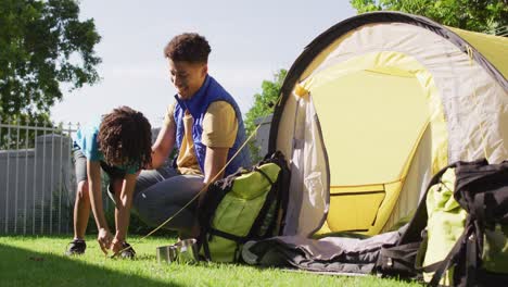 happy biracial man and his son building tent together in garden