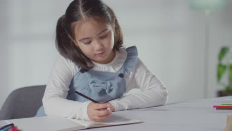 young girl on asd spectrum at table at home concentrating on writing in school book 1