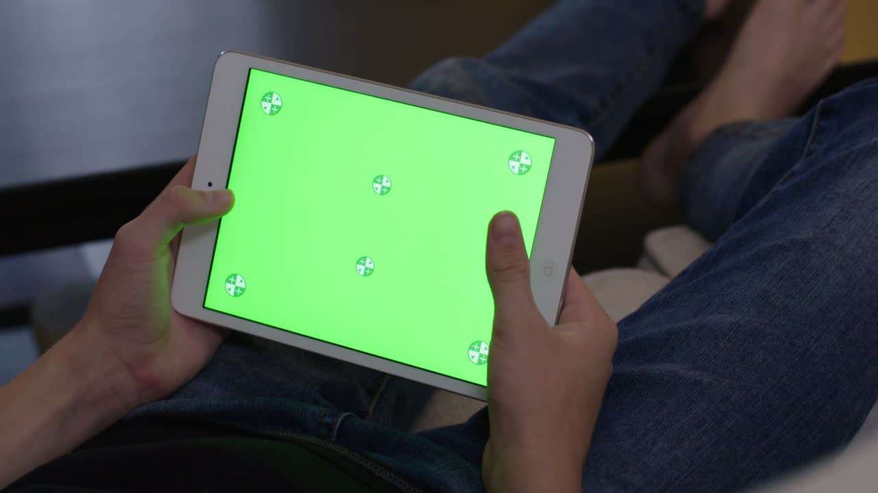 Young male sitting on sofa, male teenager at home using mobile device for homework. tablet computer monitor green screen for internet.