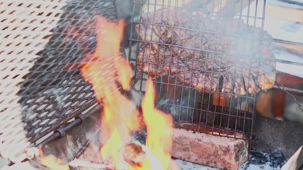 Juicy lamb rib dripping fat as it's grilled upright next to hot wood-fire