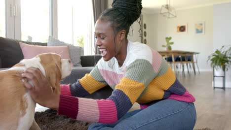 african american young woman playing with dog in living room, at home